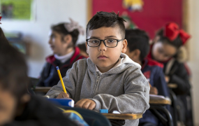 A child sitting in a classroom holding a pencil.