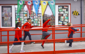Four school kids jumping in front of school building