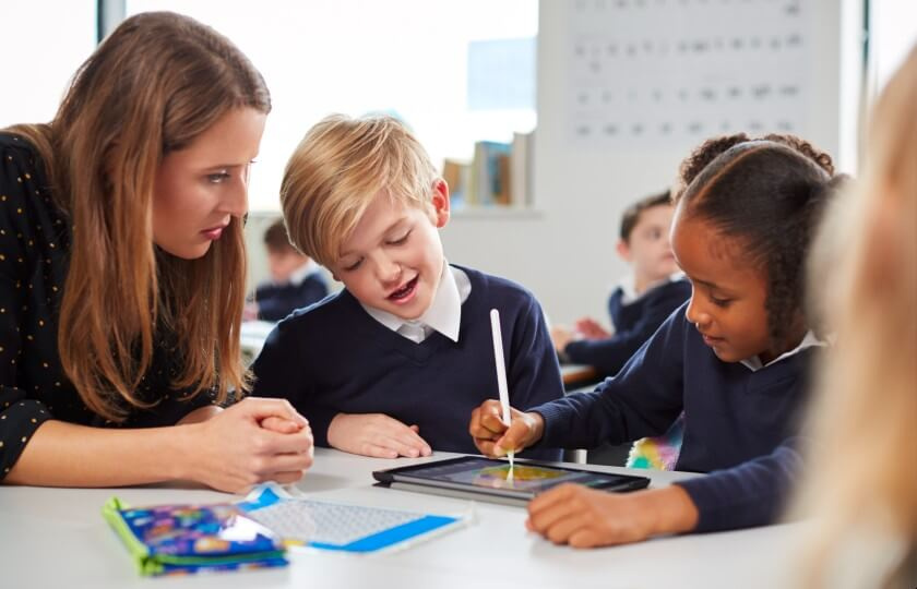 Teacher with two young students looking at a tablet.