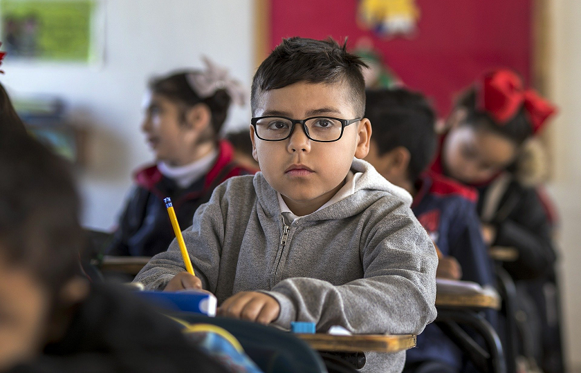 A child sitting in a classroom holding a pencil.