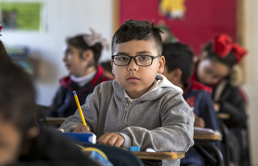 Young boy in class holding a pencil and looking straight at the camera.